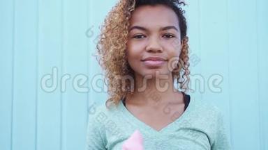 快乐的黑人女孩在蓝墙背景下缓慢移动着粉色融化的冰淇淋